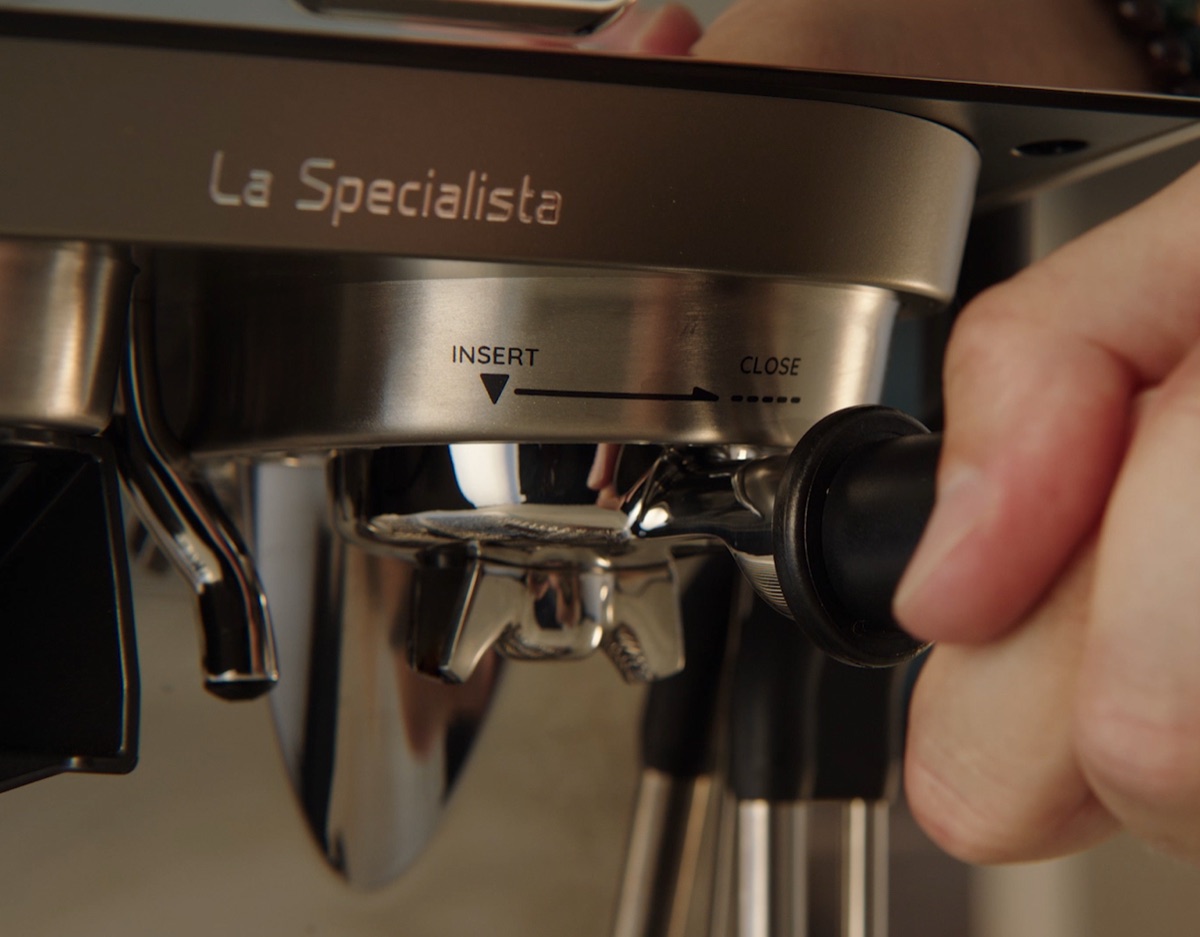 La Specialista — a hand locking the portafilter into the group head